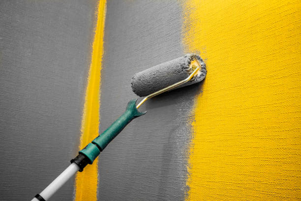 Close up roller with gray paint for painting walls. Repairs. Yellow wall. Background. Screensaver for the site. High quality photo